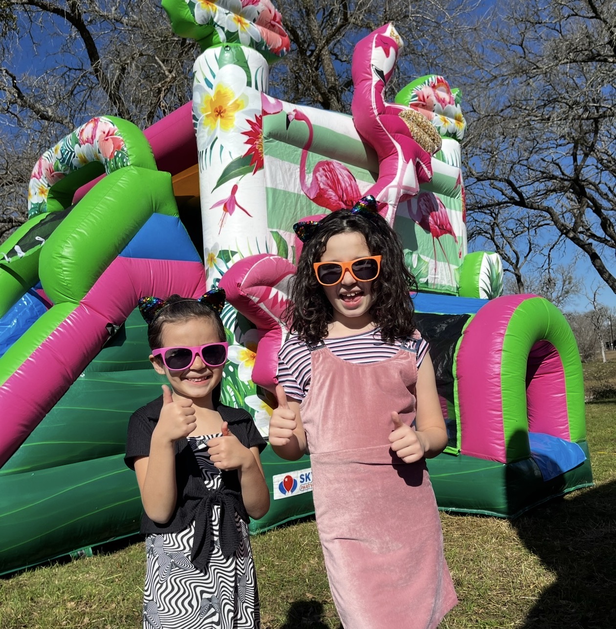 Susy and Veronica De Los Santos giving a thumbs up in front of a Sky High Party Rentals bounce house